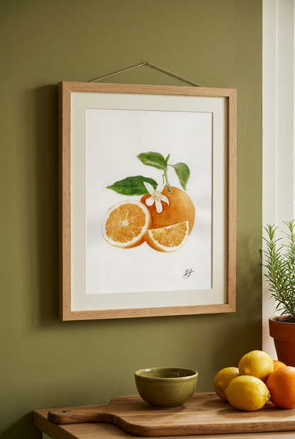 A framed watercolor print of mandarin fruit hanging on a sage green wall above a wooden table with lemons, a small bowl, and a potted plant.